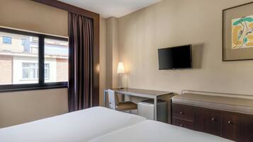 Una habitación de hotel con una cama, un escritorio con silla, una televisión y un armario.