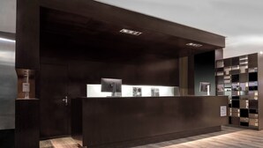A modern reception desk with a dark wood finish, a glass display case, and a sign indicating the name of the establishment. - AC Hotel Zamora by Marriott (Zamora)