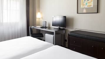 Una habitación de hotel con cama, escritorio con ordenador y lámpara, un refrigerador pequeño y un armario.