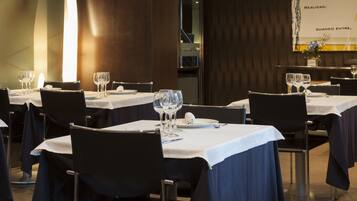 Un restaurante con varias mesas dispuestas, cubiertas con manteles blancos y sillas negras.
