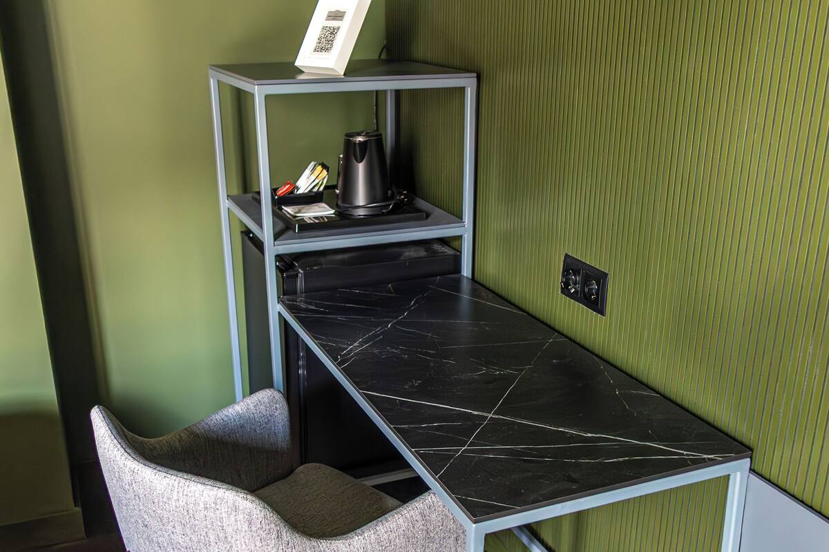 A compact workspace with a desk, chair, and shelving unit against a green wall.