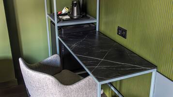 A compact workspace with a desk, chair, and shelving unit against a green wall.