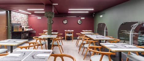 Un restaurante con mesas y sillas de madera, una máquina de café y un muro decorativo.