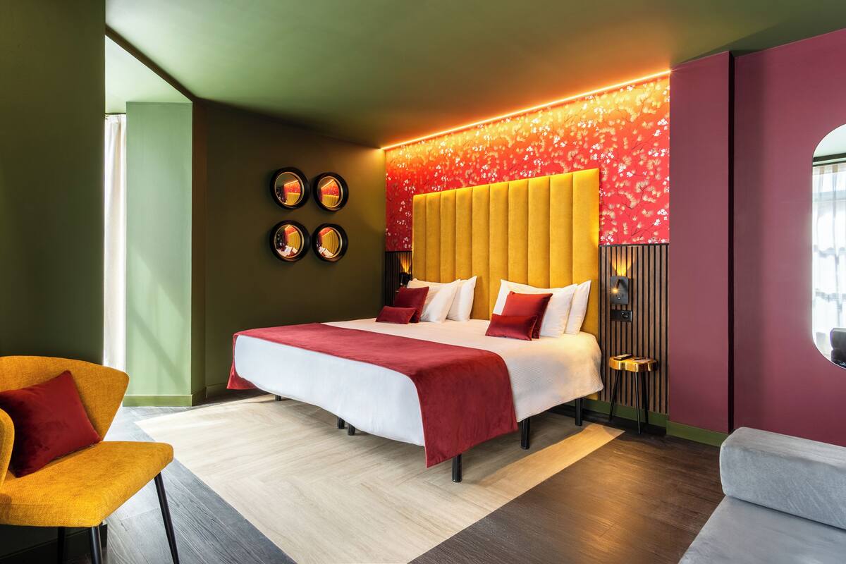 A modern hotel room with a large bed, a small stool, and a chair.