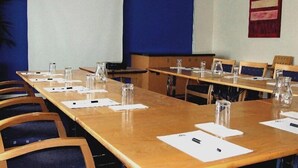 A conference room with long tables, chairs, and a projector screen. - Travelodge Derby Cricket Ground (Derby)