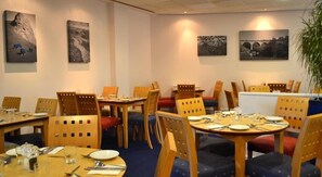 A dining area with wooden tables and chairs, some with red cushions. There are paintings on the walls. - Travelodge Derby Cricket Ground (Derby)