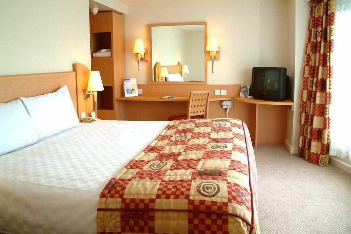 A hotel room with a bed, a desk, a television, and a mirror.