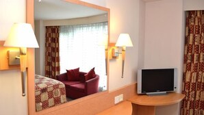 A hotel room with a large mirror, two bedside lamps, a TV on a wooden stand, and a red sofa with patterned cushions. - Travelodge Derby Cricket Ground (Derby)