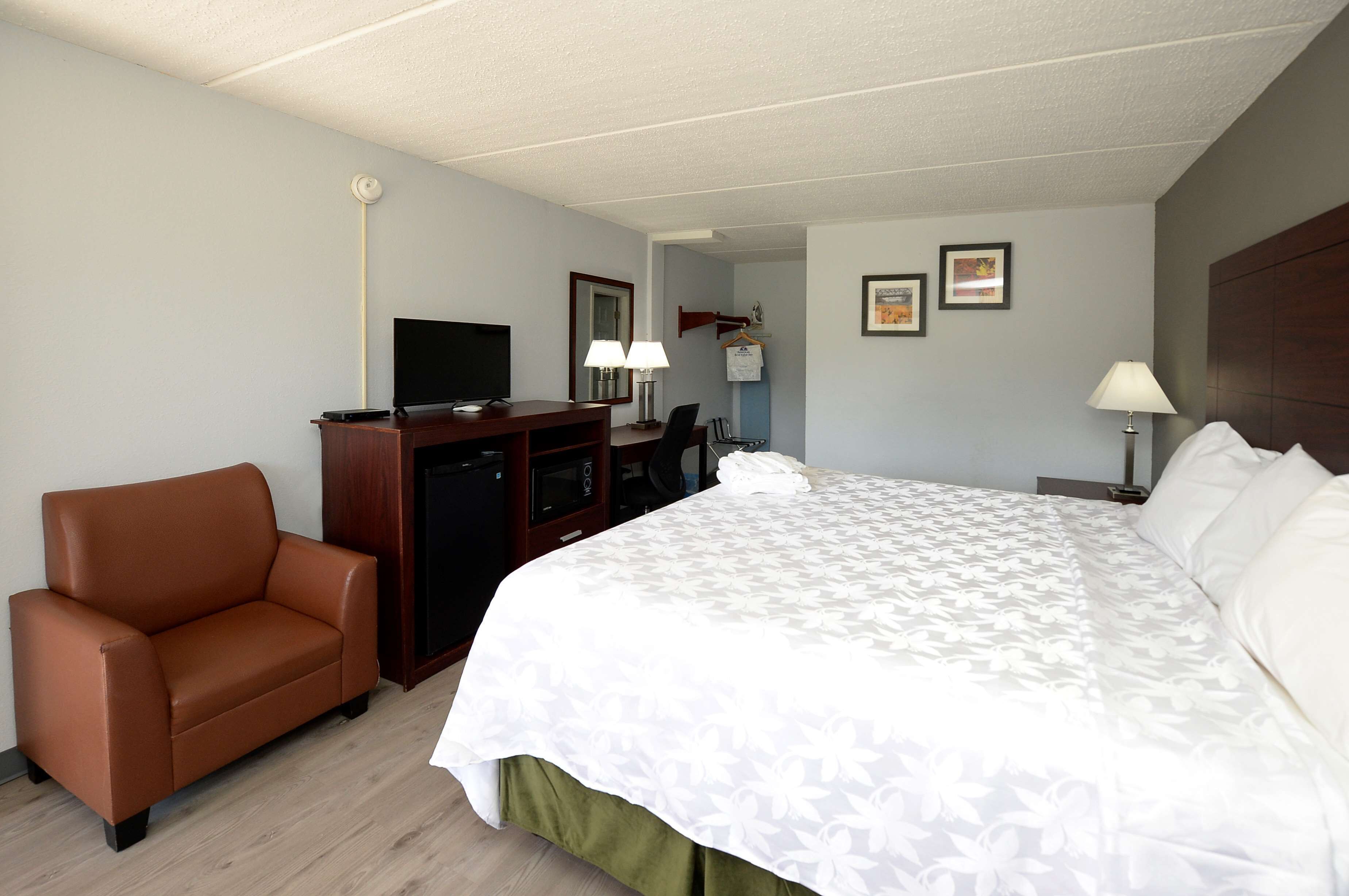 A hotel room with a bed, a desk, a chair, a television, and a coat rack.