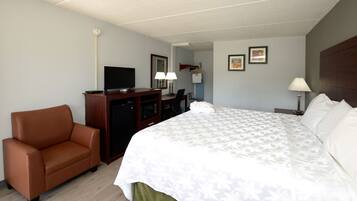A hotel room with a bed, a desk, a chair, a television, and a coat rack.