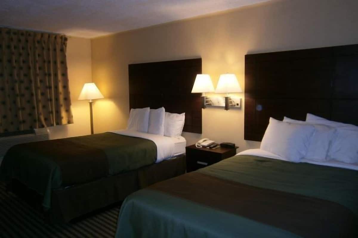 Habitación de hotel con dos camas, cada una con cabecera, lámparas de noche y teléfono en la mesita.