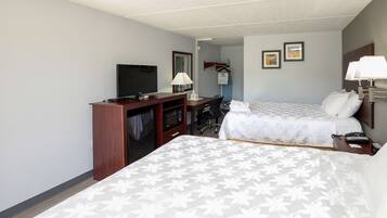 Quarto de hotel com duas camas, uma escrivaninha com televisão, uma lâmpada e um cabideiro.