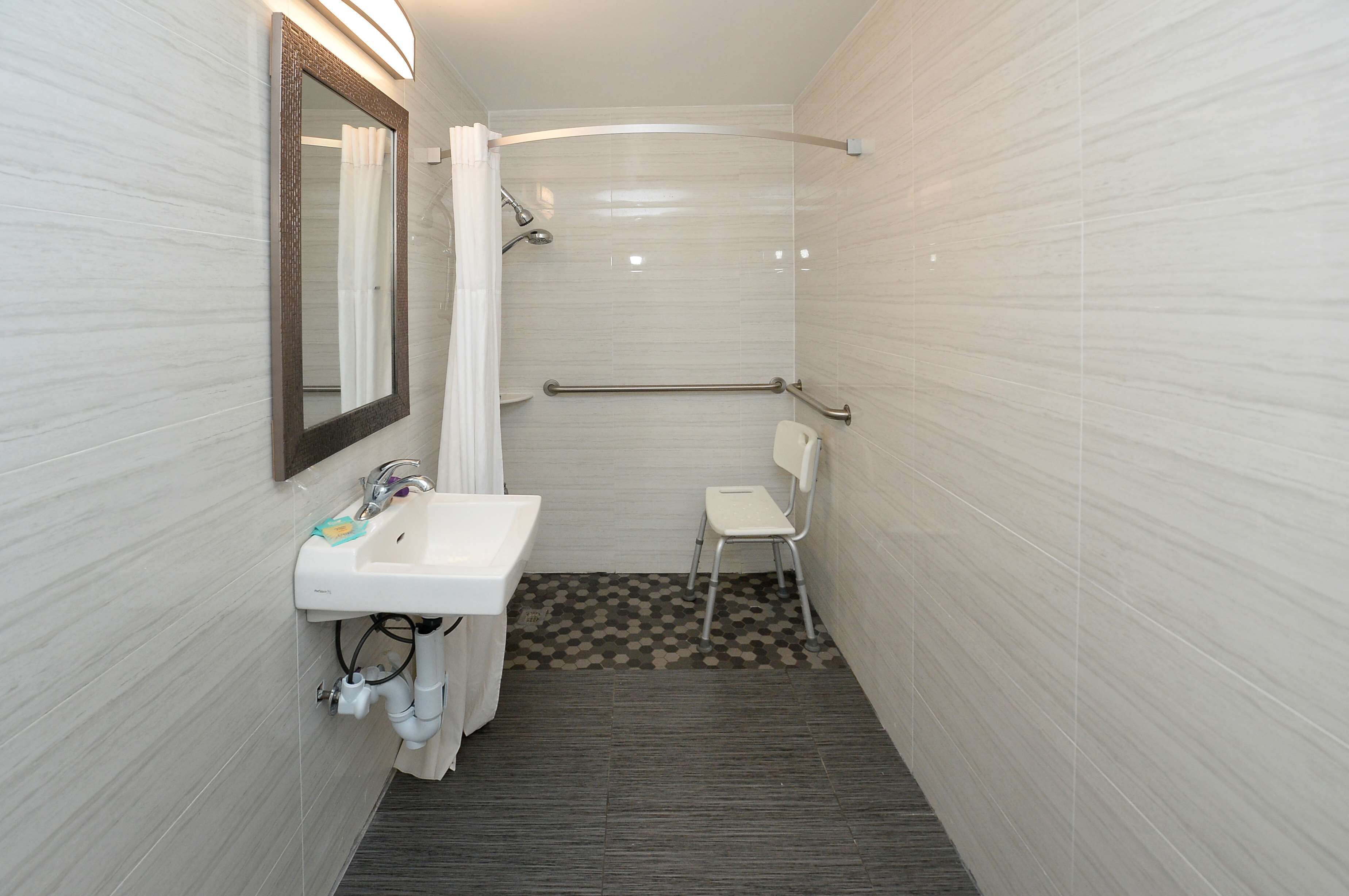 Un baño pequeño y moderno con un lavamanos blanco, un espejo, una ducha y una silla.