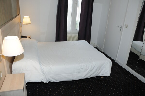 Una habitación de hotel con una cama, una mesita de noche, una lámpara, un teléfono y una ventana con cortinas.