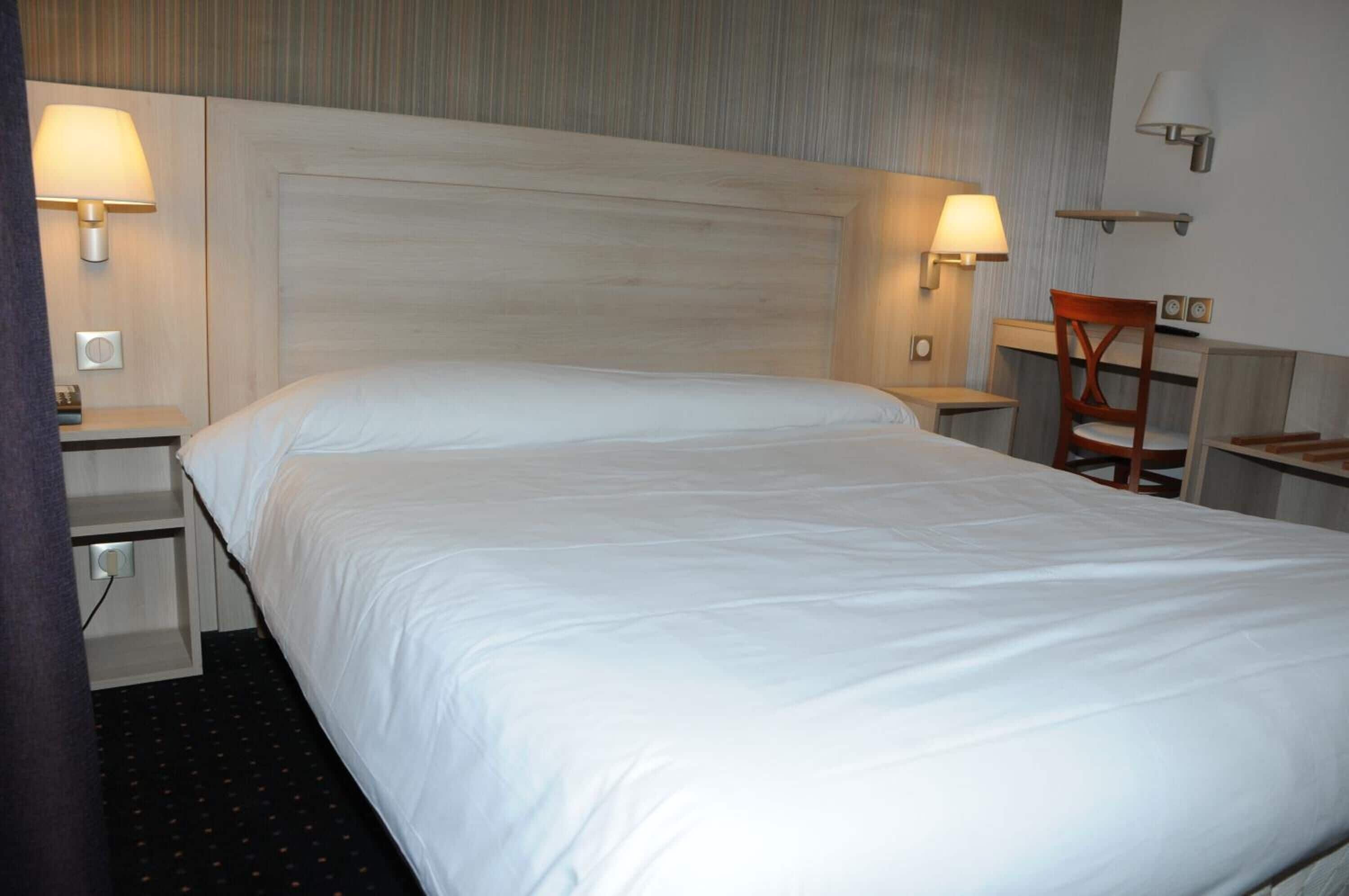 A hotel room with a large bed, two bedside tables with lamps, a wooden chair, and a small desk with a chair.