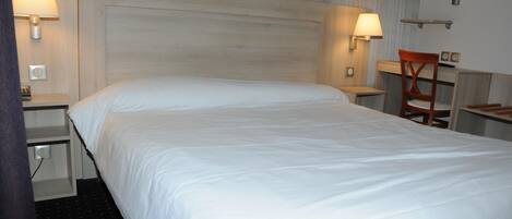 A hotel room with a large bed, two bedside tables with lamps, a wooden chair, and a small desk with a chair.