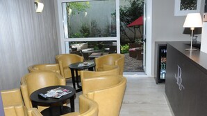 Un moderno vestíbulo de hotel con sillones y mesas de cuero, un mostrador de recepción y vistas al patio exterior.