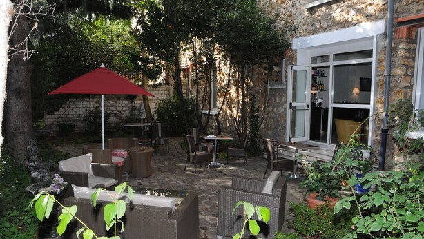 Un patio al aire libre con muebles de mimbre, un paraguas rojo y una pared de piedra.