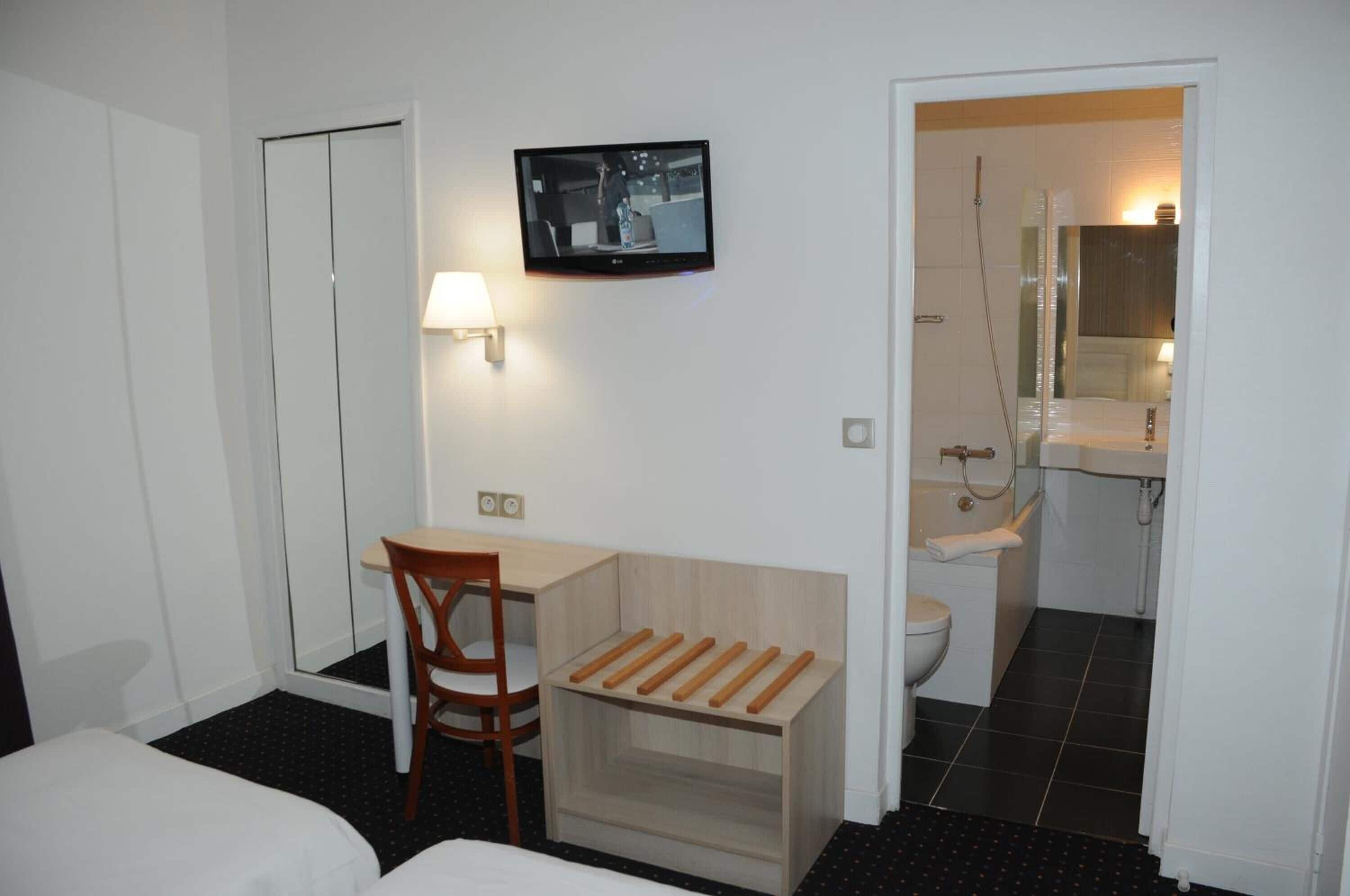 A hotel room with a bed, a desk with a chair, a television, a mirror, and a bathroom with a toilet and sink.