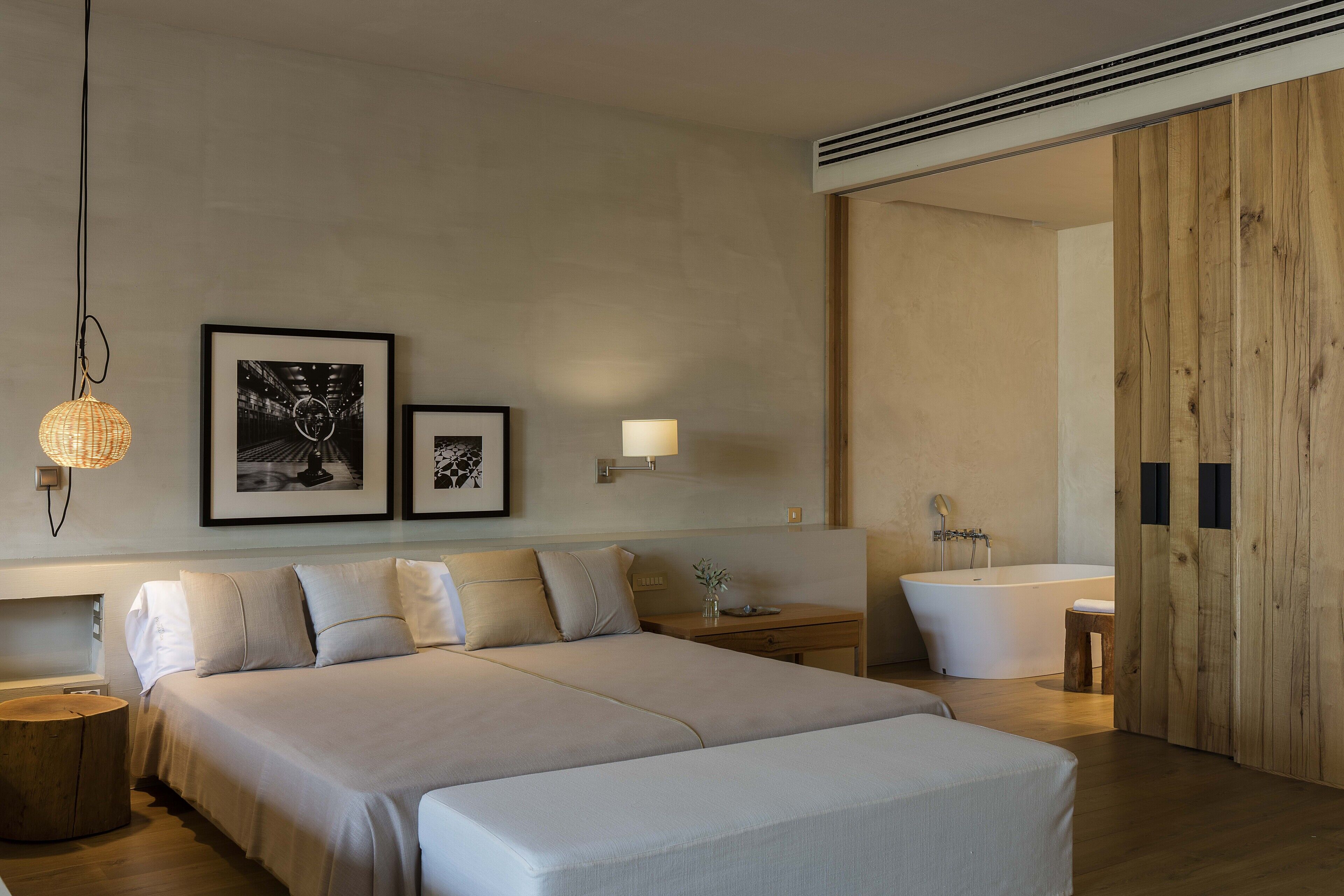 Une chambre d’hôtel moderne avec un grand lit, une table de chevet, une lampe et une porte en bois donnant accès à la salle de bain.