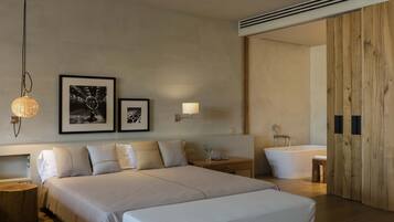 Une chambre d’hôtel moderne avec un grand lit, une table de chevet, une lampe et une porte en bois donnant accès à la salle de bain.
