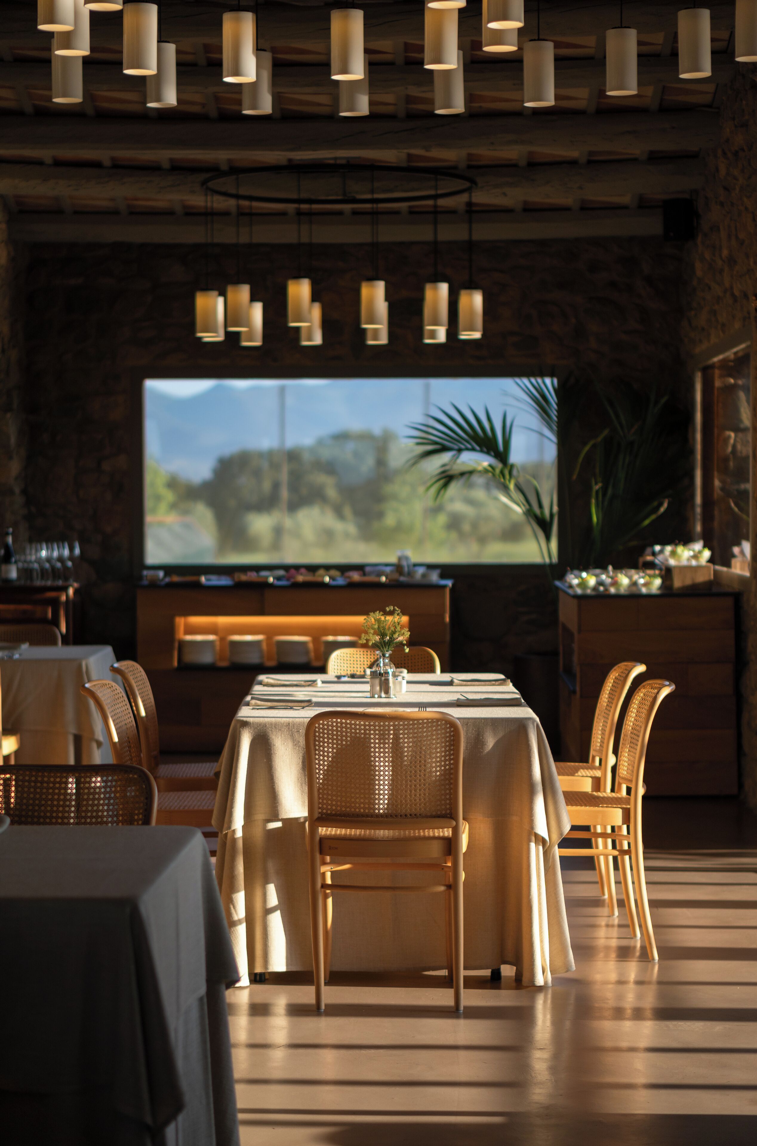 A restaurant with a large TV screen, wooden furniture, and hanging pendant lights.