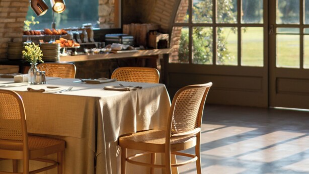 A dining area with a brick arch ceiling, a table set for two, and a view of the outdoors through large windows.