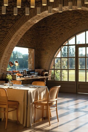 A dining area with a brick arch ceiling, a table set for two, and a view of the outdoors through large windows. - Hotel Peralada Wine Spa & Golf (Perelada)
