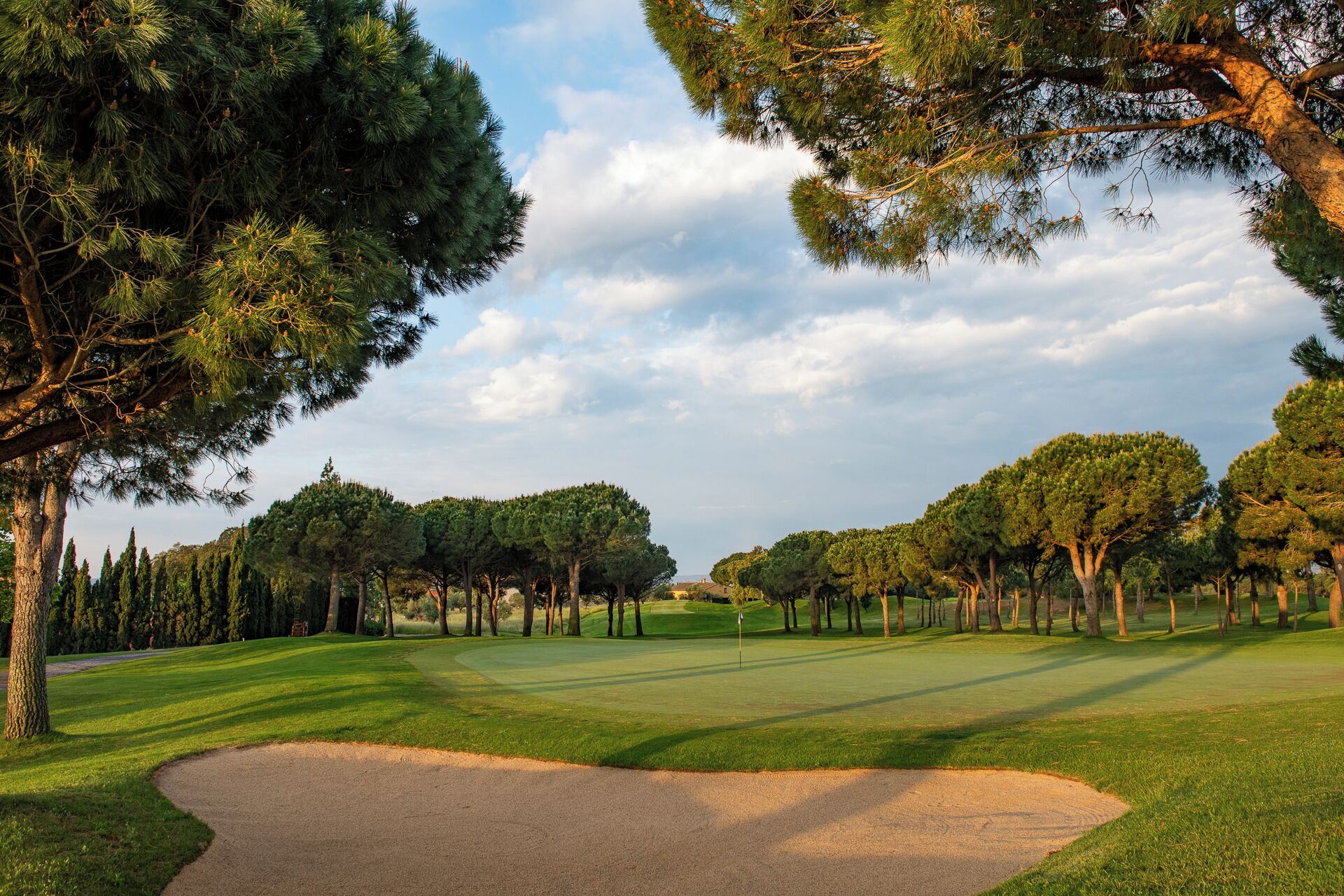 Campo de golf con un búnker de arena, árboles y cielo despejado.