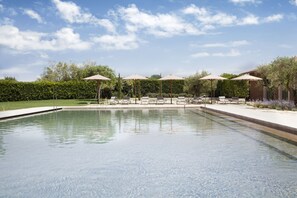 A swimming pool with lounge chairs and umbrellas, surrounded by greenery and a clear sky. - Hotel Peralada Wine Spa & Golf (Perelada)