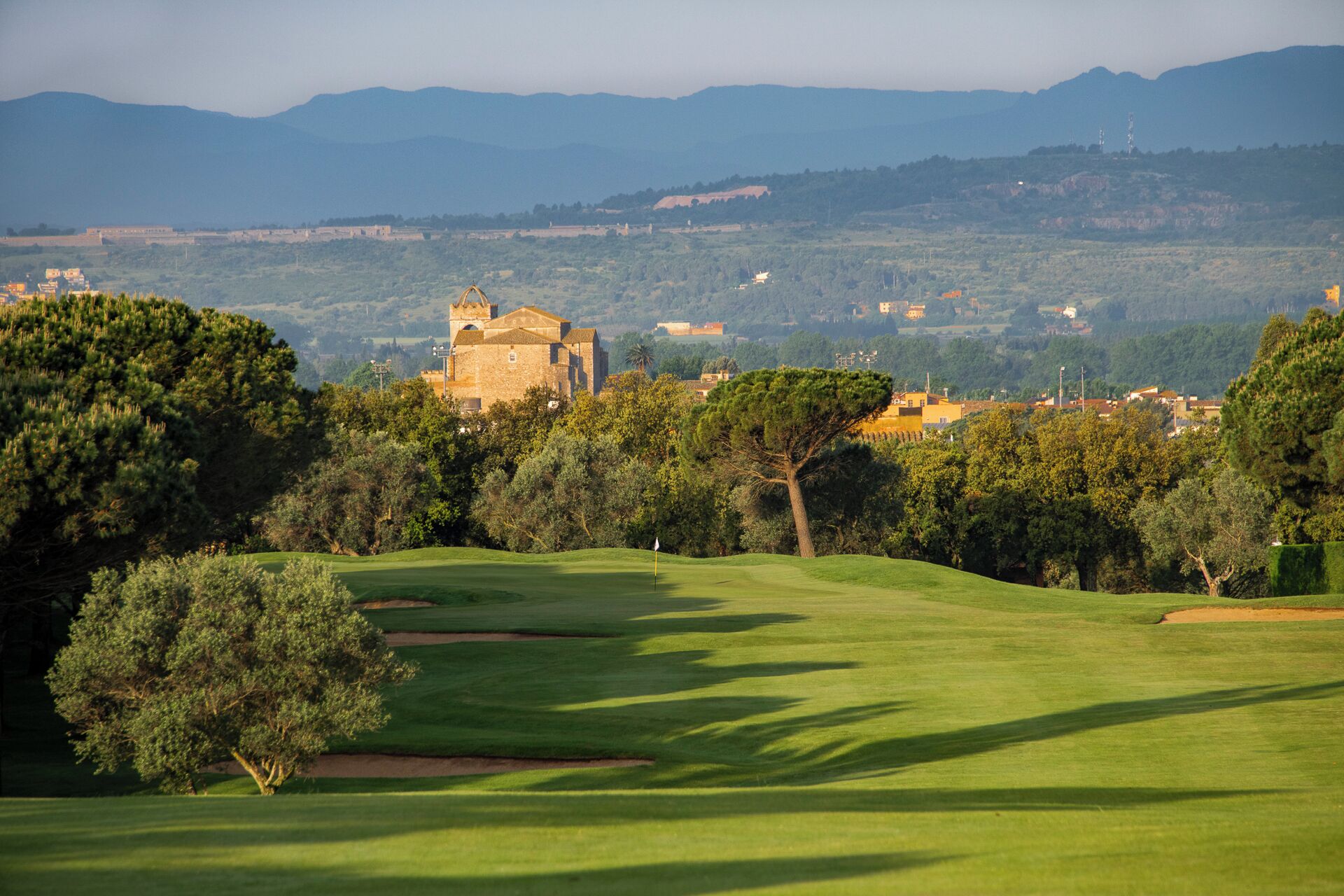 Un campo de golf con un castillo al fondo, rodeado de árboles y colinas.