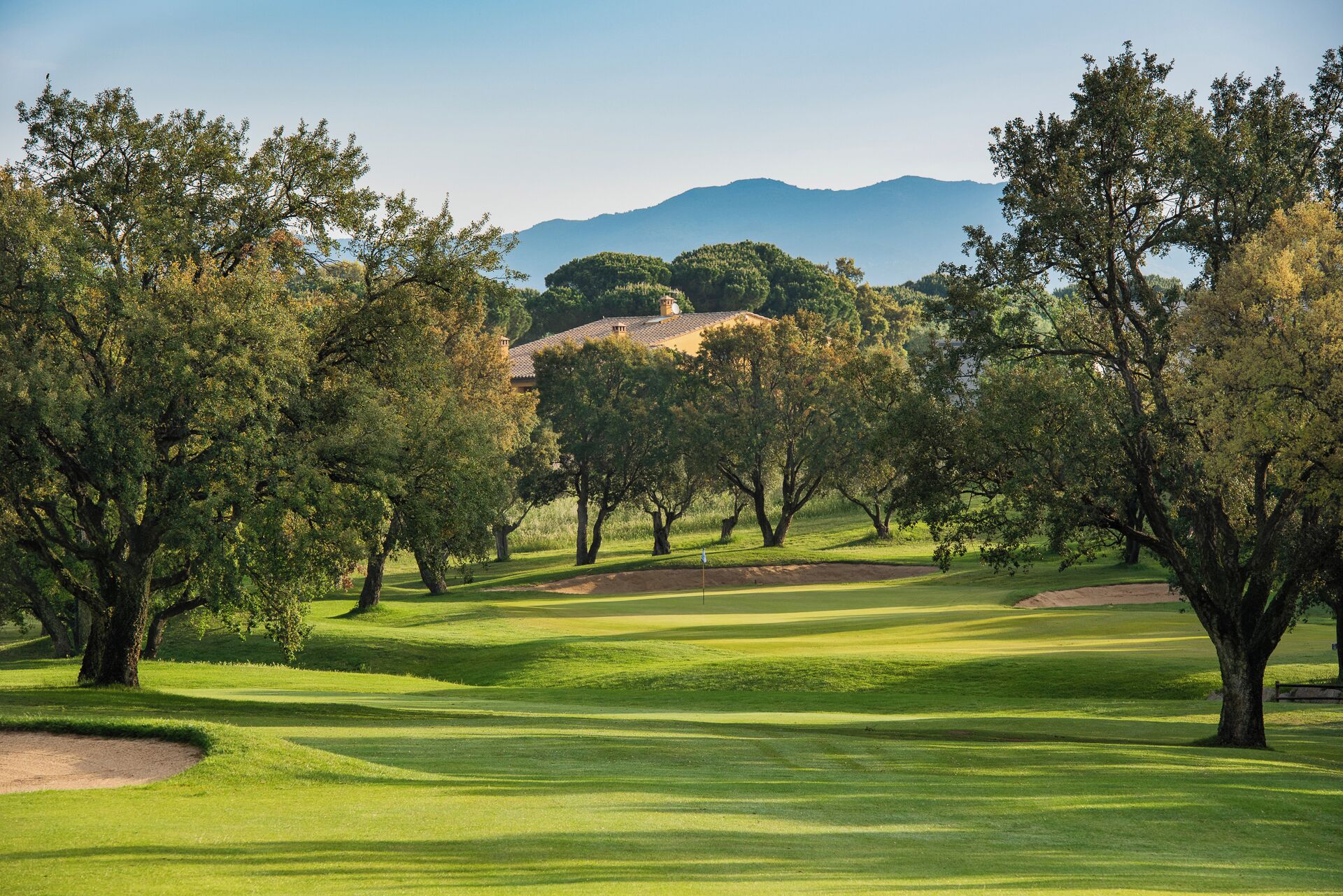 A golf course with trees, a clear sky, and distant mountains.