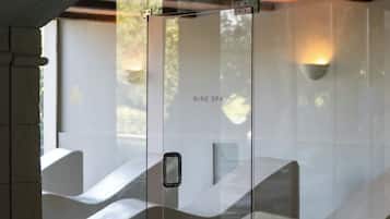 Un spa modern amb una porta de vidre, seients de pedra i un sòl de fusta.