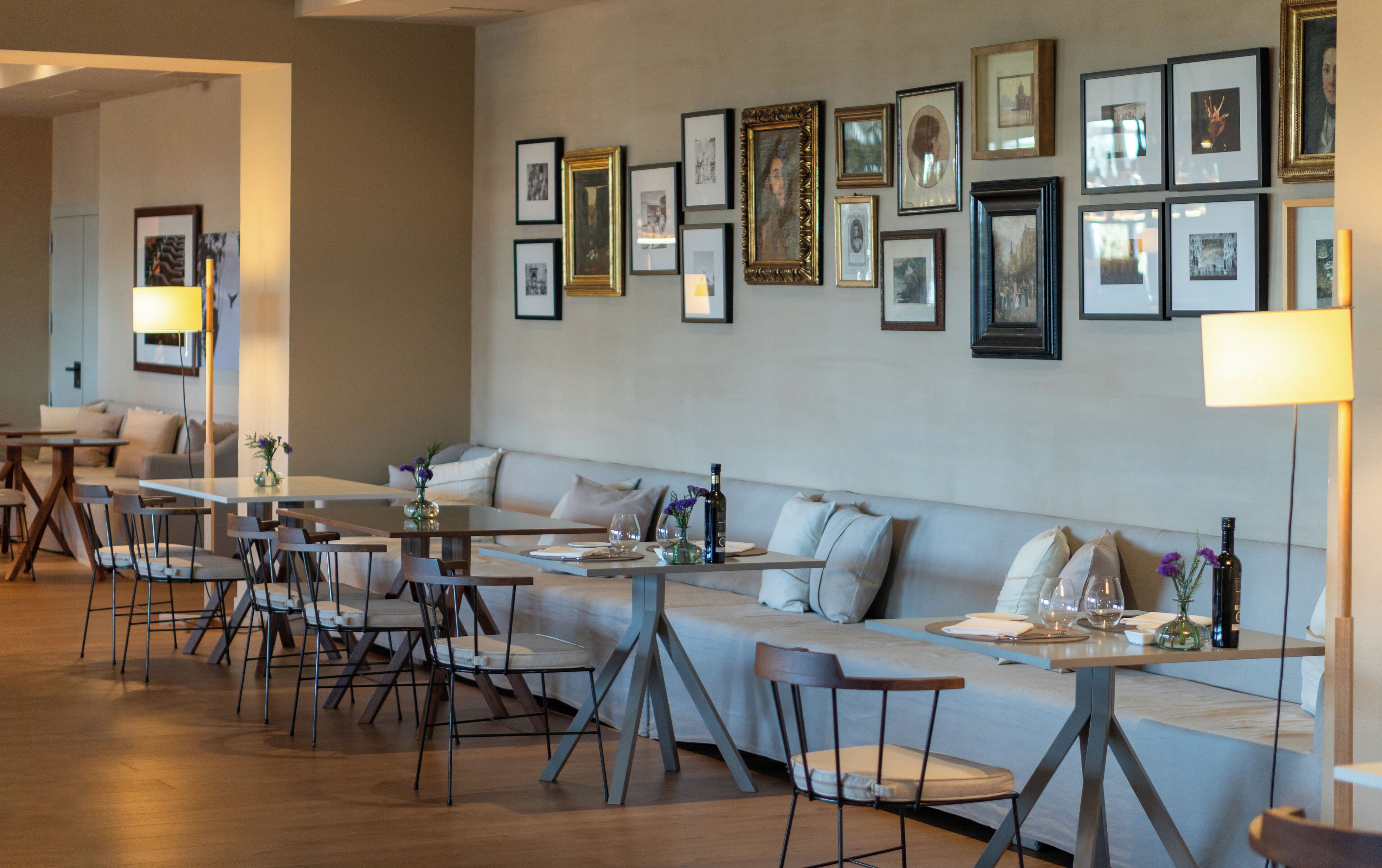 Un espace repas moderne avec une longue table, plusieurs chaises, un canapé et un mur décoré de tableaux encadrés.
