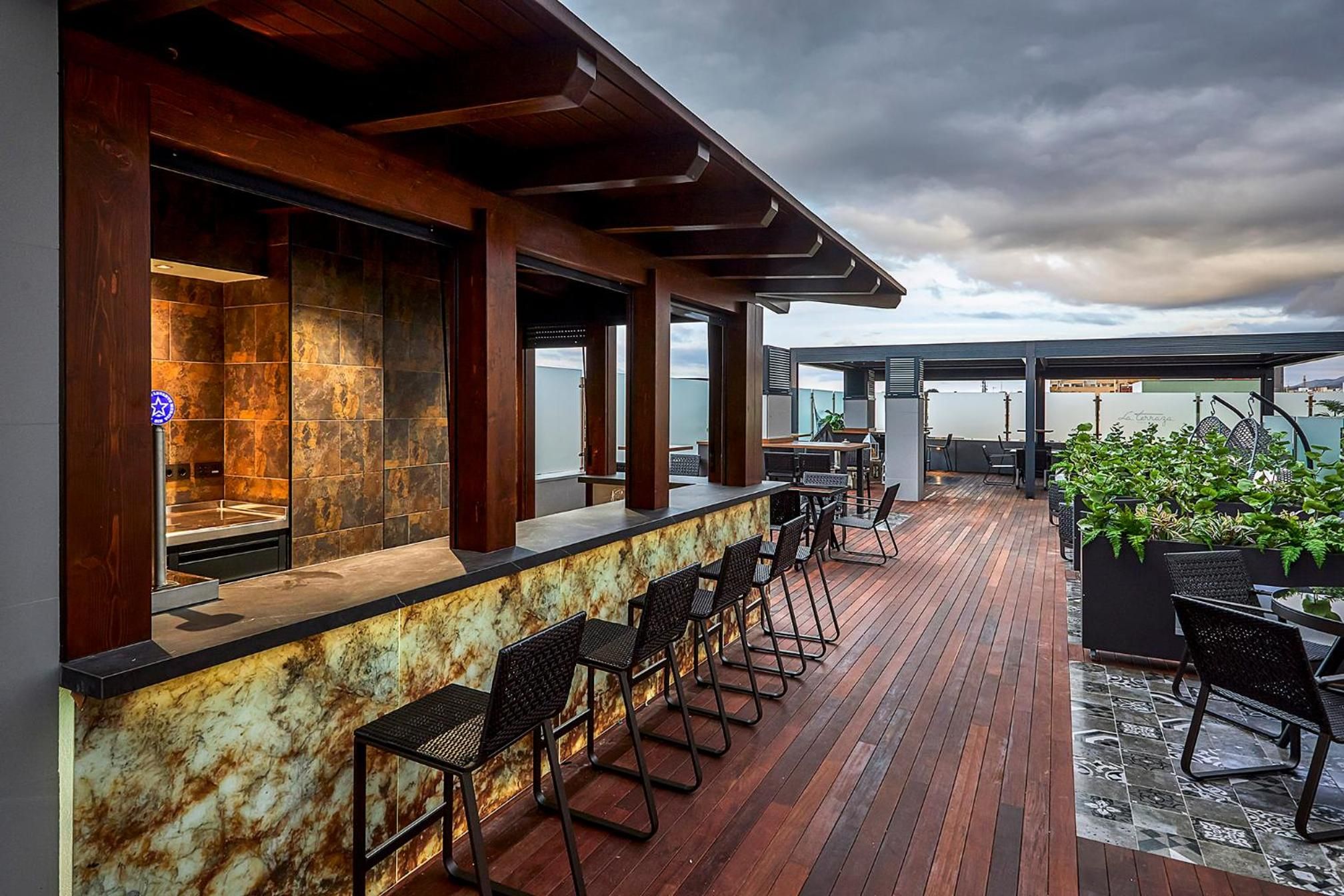 Un bar al terrat amb terrassa de fusta, tamborets i seients exteriors.