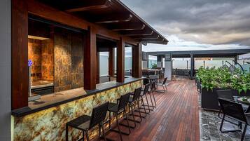Un bar al terrat amb terrassa de fusta, tamborets i seients exteriors.