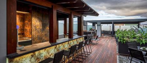 Un bar en la azotea con terraza de madera, taburetes y asientos al aire libre.