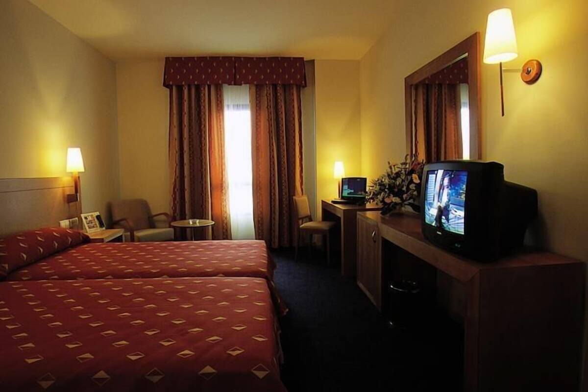 A hotel room with two beds, a desk with a computer, a television, and a lamp.