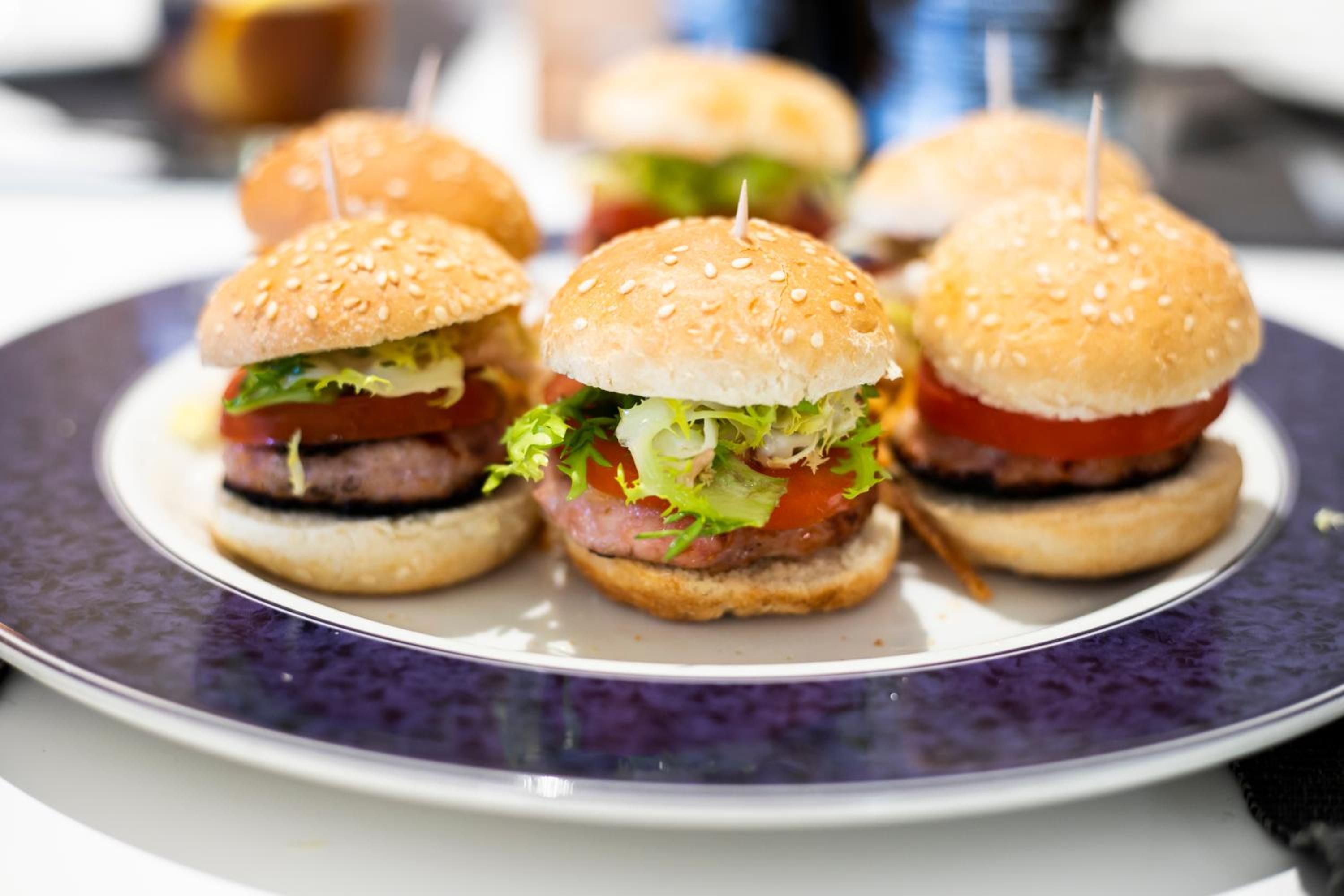 Un plato con cuatro hamburguesas pequeñas, cada una con un panecillo de sésamo, lechuga, tomate y una hamburguesa de carne.