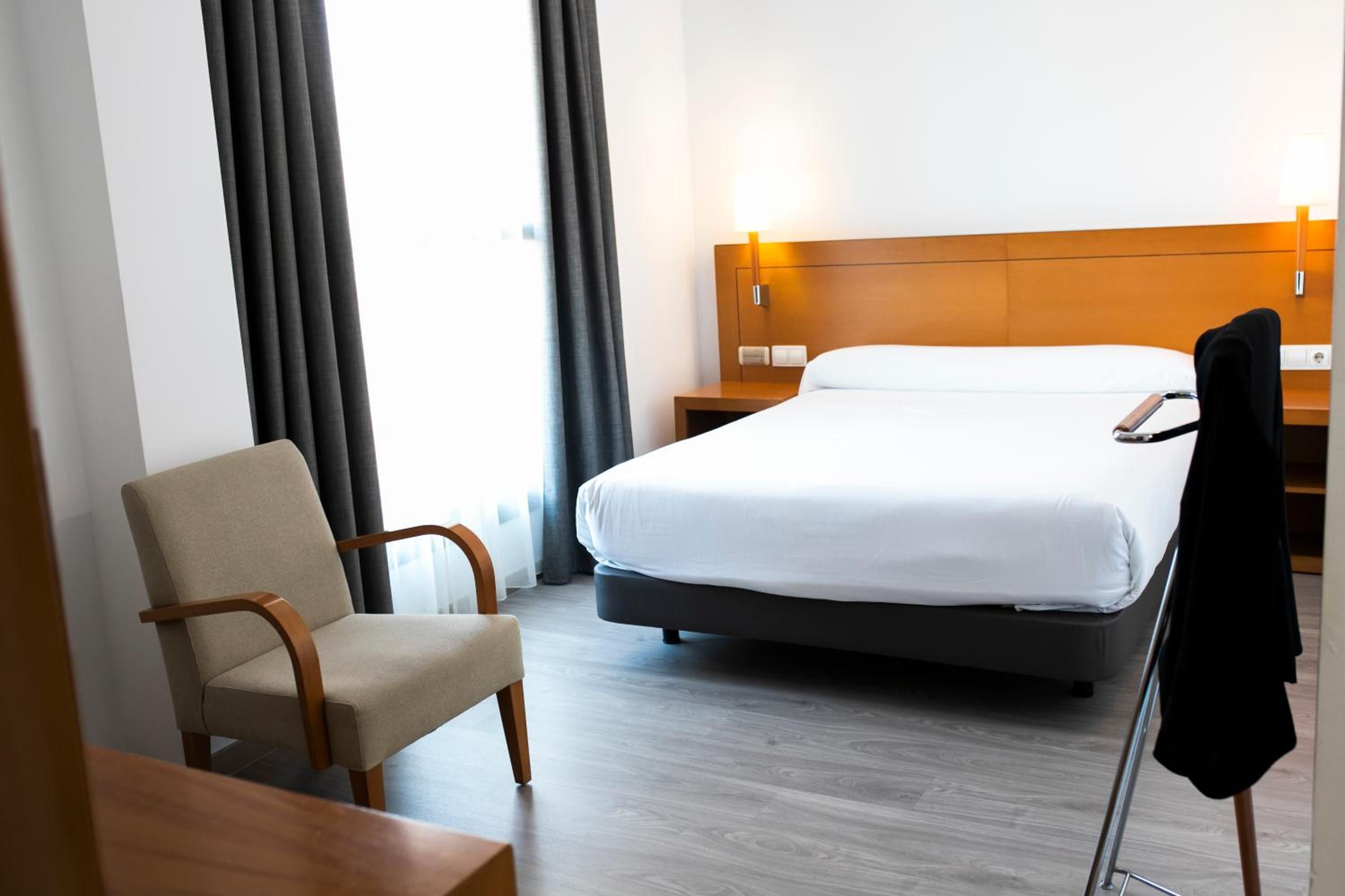 A hotel room with a bed, a chair, a nightstand, and a lamp.
