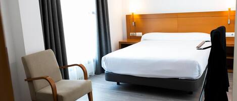 A hotel room with a bed, a chair, a nightstand, and a lamp.