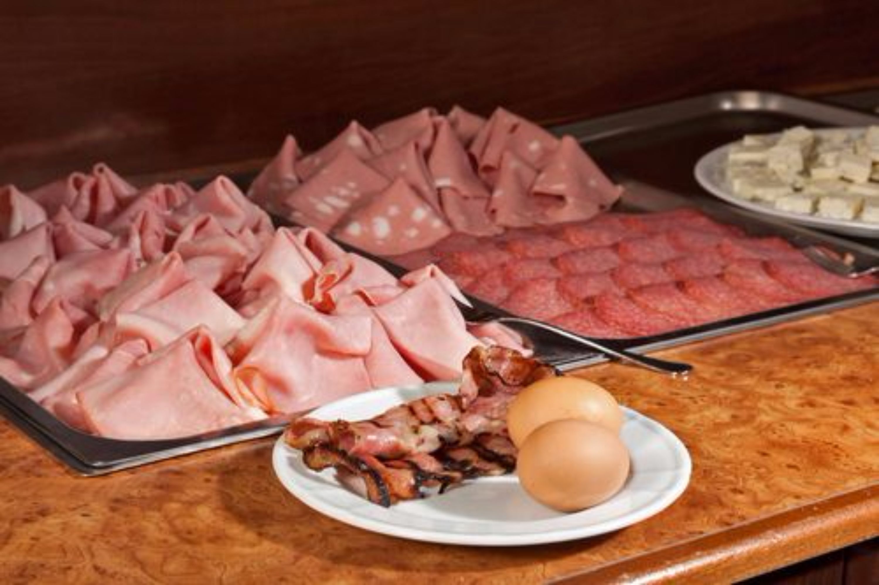 A buffet with various meats and a plate with bacon and eggs.