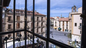 Visão de uma praça histórica, com edifícios tradicionais, varandas e um campanário.