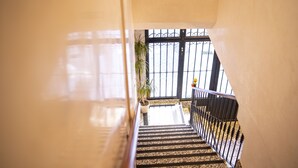 Uma escadaria com guarda-mão de metal leva a uma varanda com vista para um edifício com janelas gradeadas.