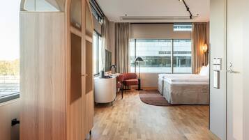 A modern hotel room with a large window, a bed, a desk, and a chair.