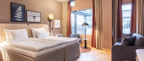 Una habitación de hotel moderna con una cama grande, un sofá, un escritorio y vistas a la ciudad.
