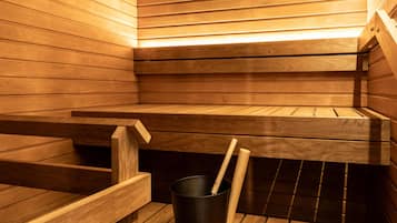 A sauna with wooden benches and a black bucket with a wooden stick.
