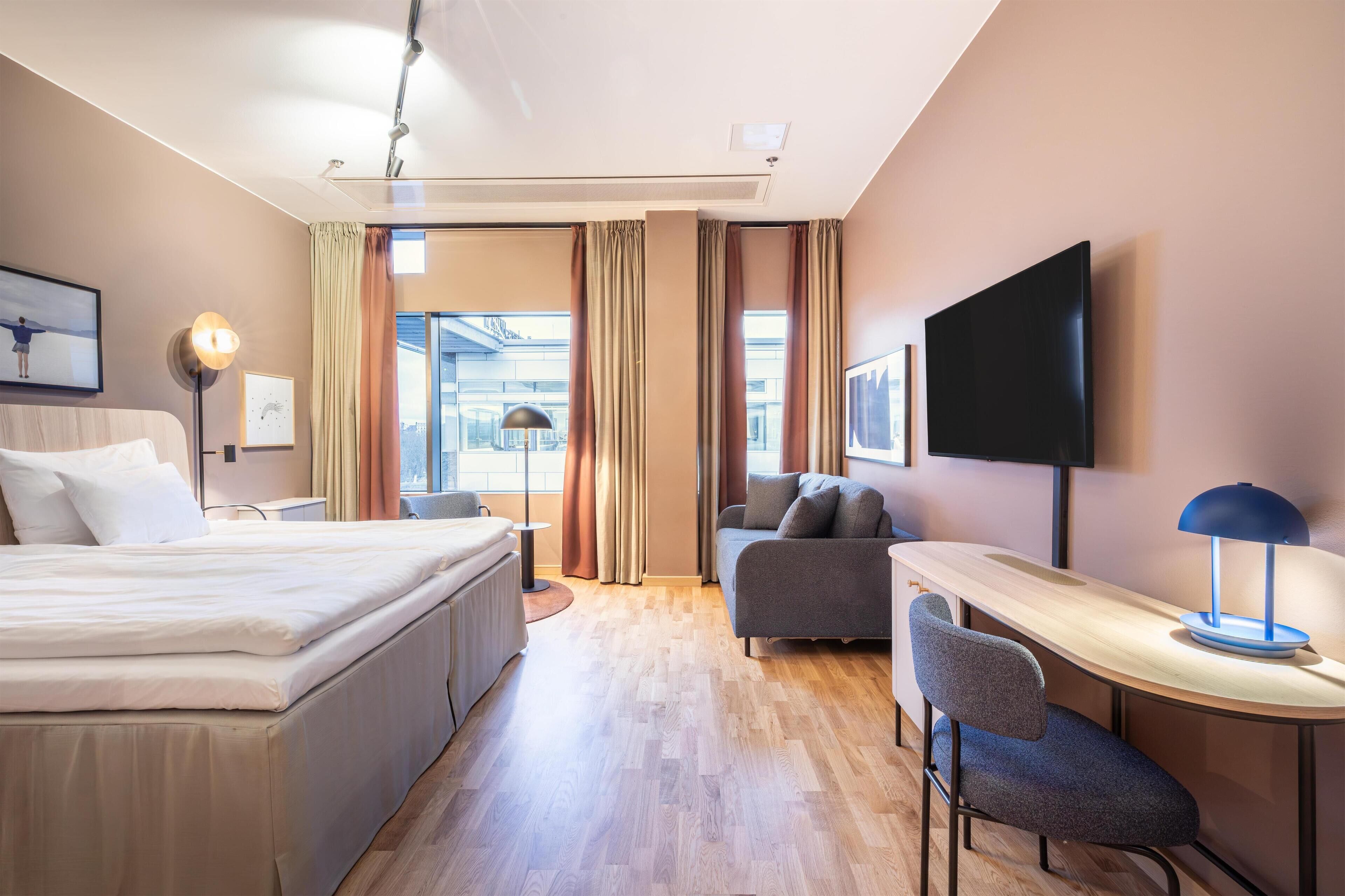 Una habitación de hotel con cama, sofá, escritorio y televisión.