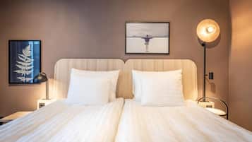 A double bed with white linens, two bedside tables, a framed artwork of a person with arms outstretched, a floor lamp, and a wall-mounted picture of a fern.