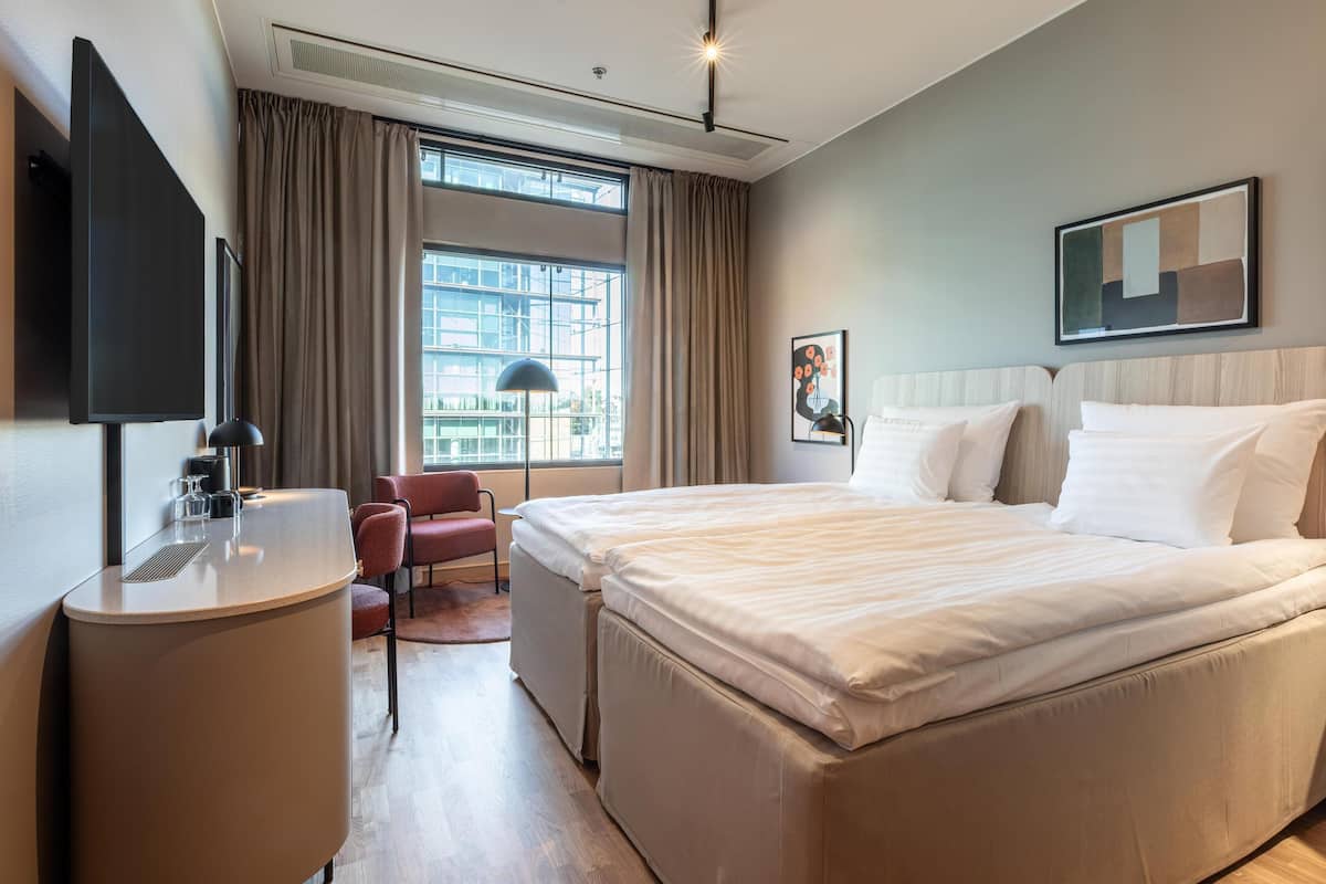A modern hotel room with a large bed, a desk, a chair, and a TV.